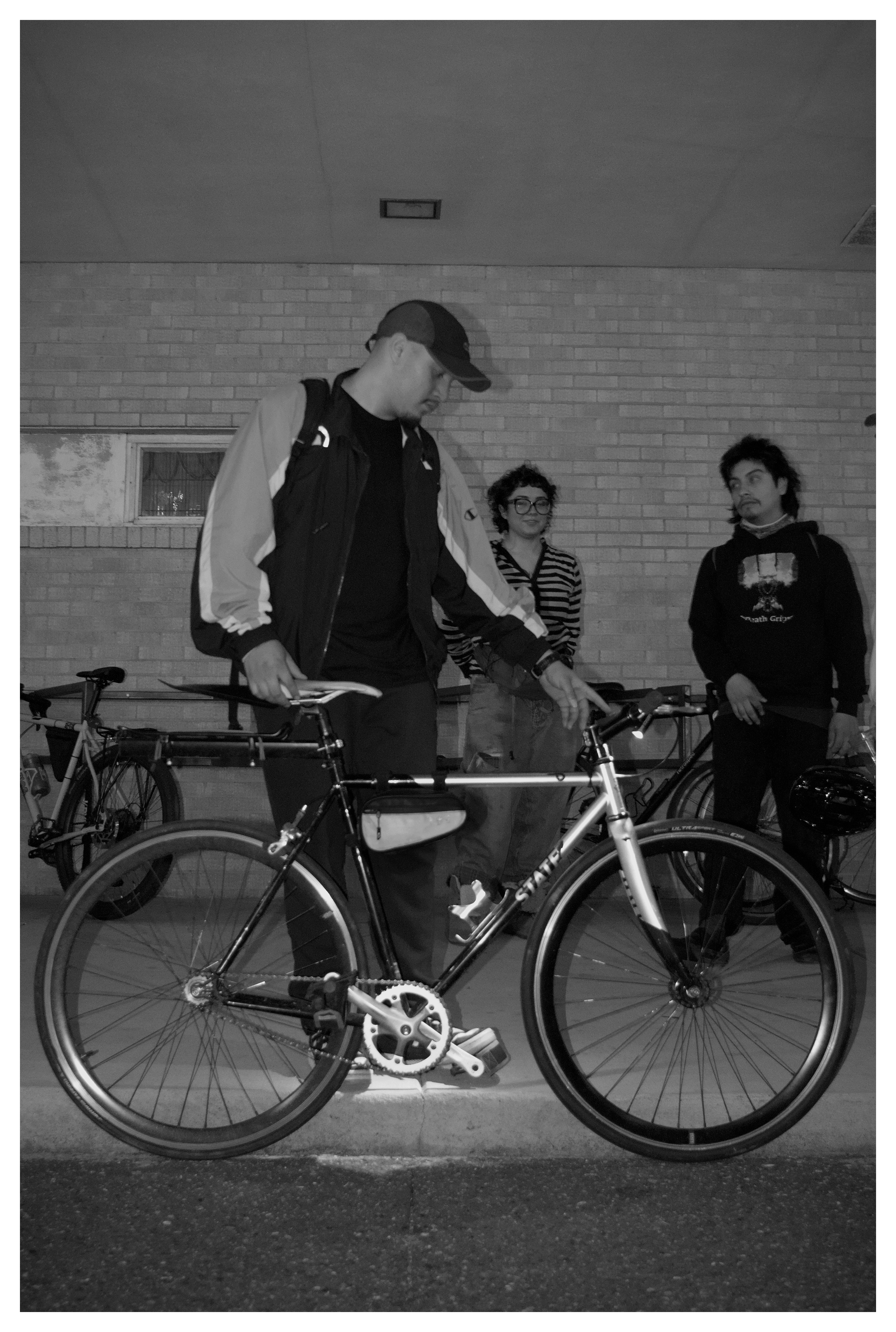 a person looking down at their bike, with two people in the background